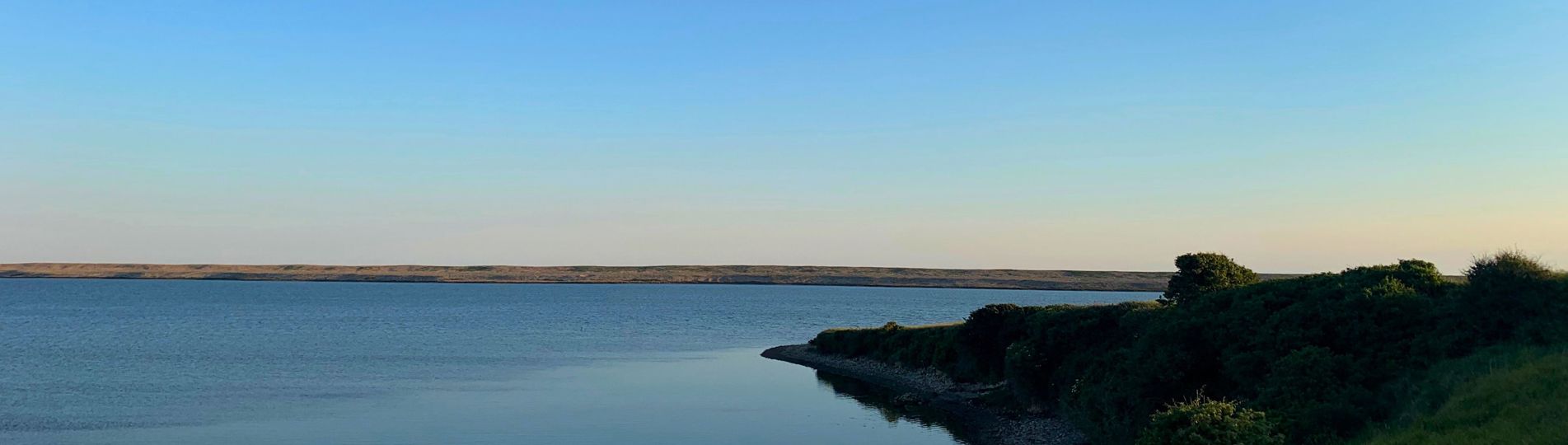 Fleet Lagoon at sunset with calm blue water and Chesil Beach in the background