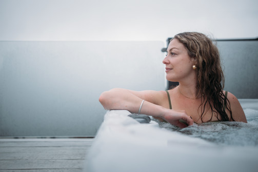 A woman in a hot tub looking out towards the view on the decking of a lodge