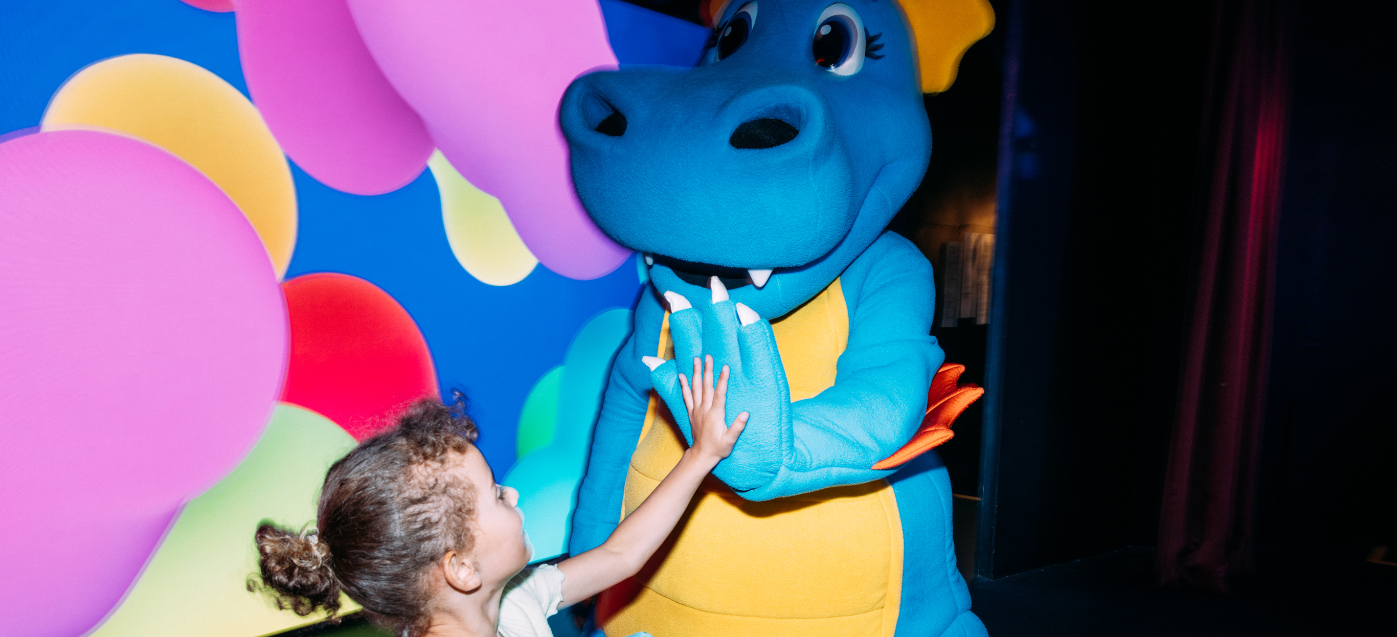 A dinosaur mascot, Vic, on stage with a young girl high-fiving