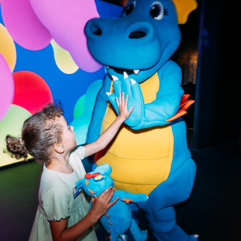 A dinosaur mascot, Vic, on stage with a young girl high-fiving