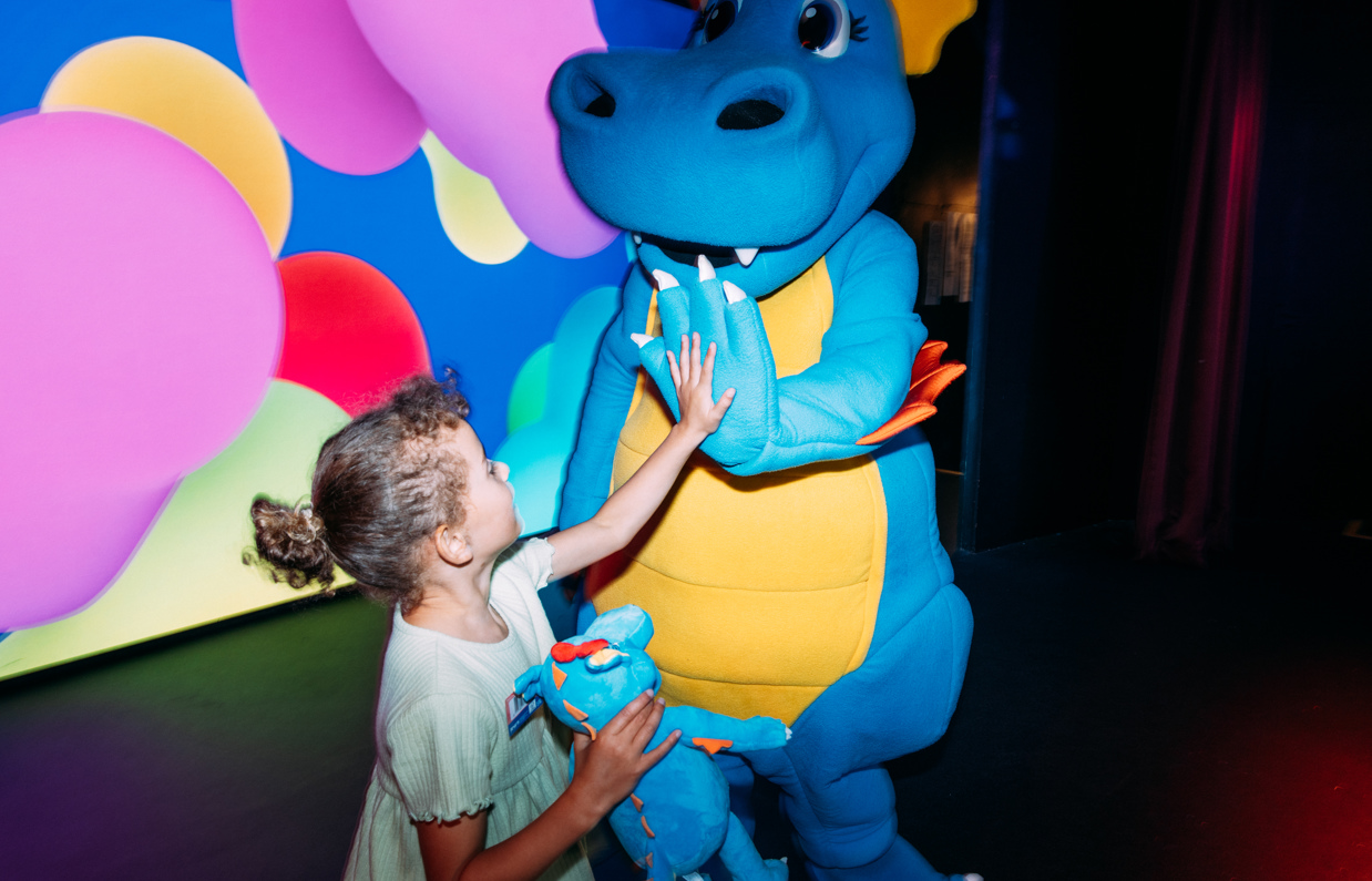 A dinosaur mascot, Vic, on stage with a young girl high-fiving