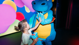 A dinosaur mascot, Vic, on stage with a young girl high-fiving