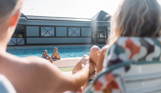 A young girl and boy in an outdoor pool with a mum and dad sat on sun loungers in the sun