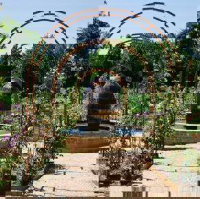 A garden of flowers and plants with arches leading to a water feature