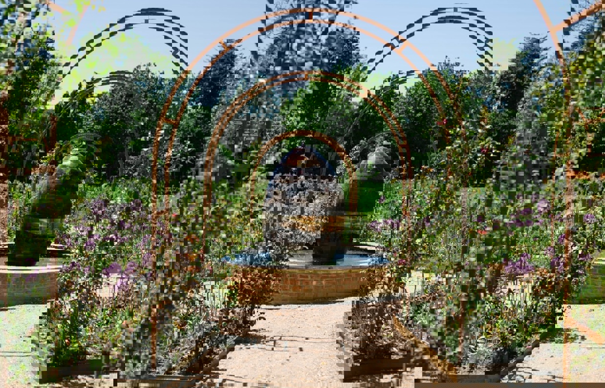 A garden of flowers and plants with arches leading to a water feature