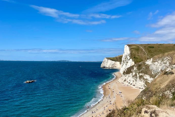 The view of Durdle Door Beach and beyond on a striking sunny, blue sky day with blue water