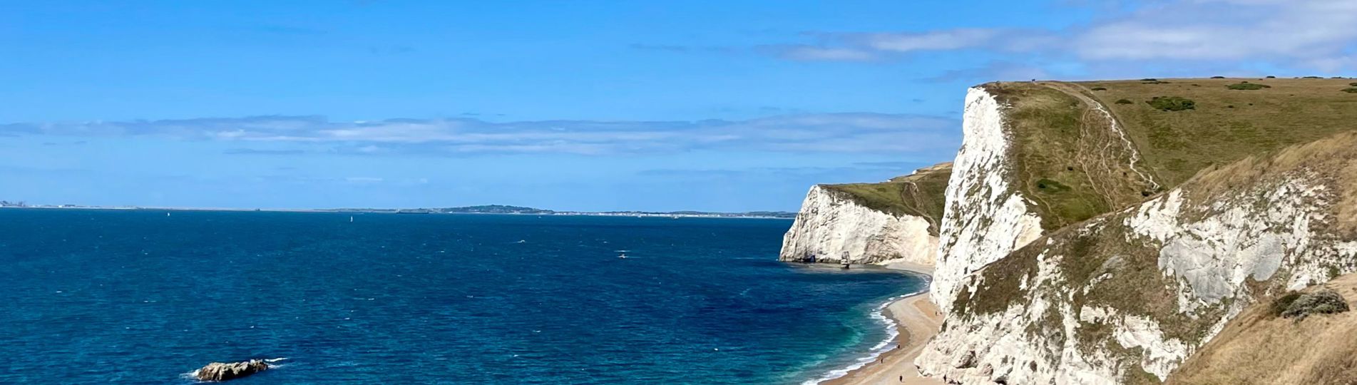 The view of Durdle Door Beach and beyond on a striking sunny, blue sky day with blue water