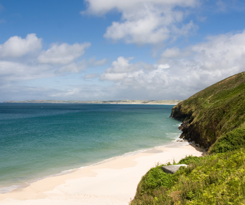 A sandy stretch of beach with grassy headland and countryside and sea views