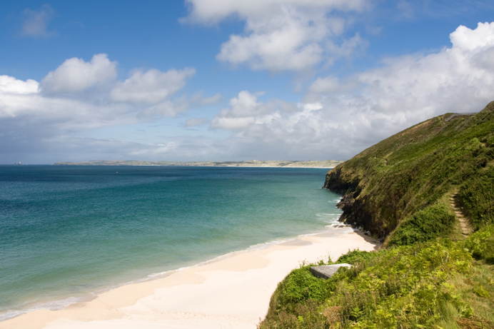 A sandy stretch of beach with grassy headland and countryside and sea views