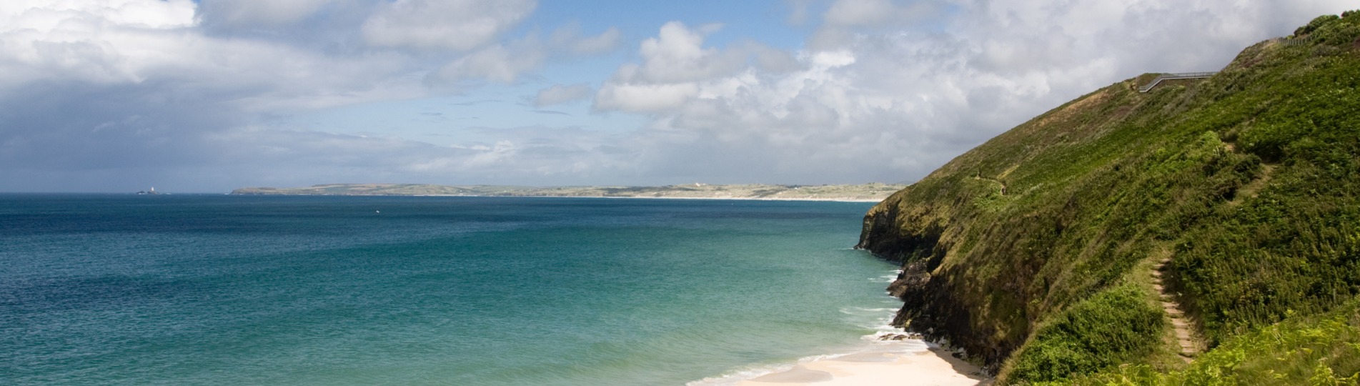 A sandy stretch of beach with grassy headland and countryside and sea views