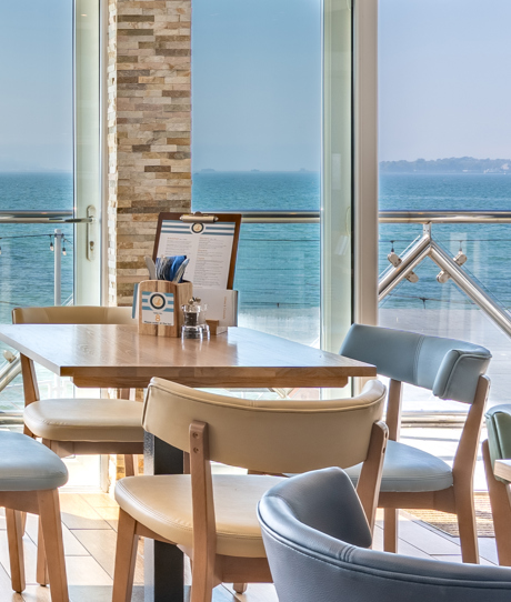 An up close shot of seating in Drift Bar & Grill with views of the sea and Weymouth Bay on a sunny, blue sky day