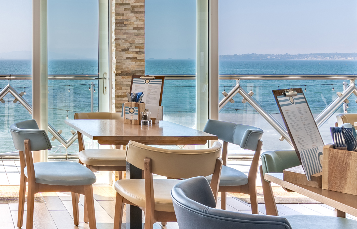 An up close shot of seating in Drift Bar & Grill with views of the sea and Weymouth Bay on a sunny, blue sky day
