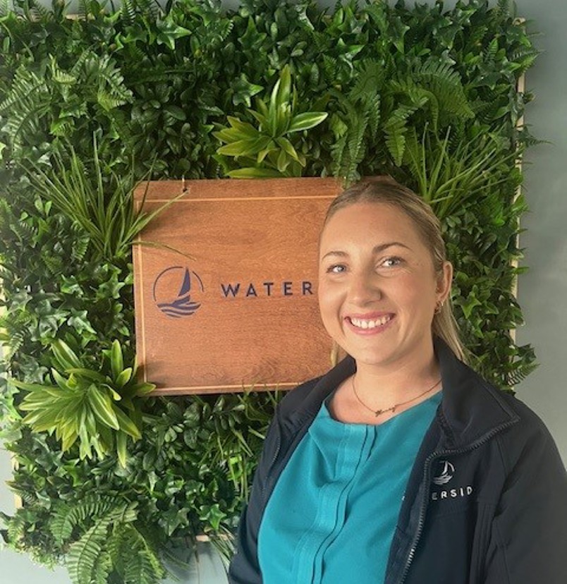 A smiling lady stood beside a Waterside sign