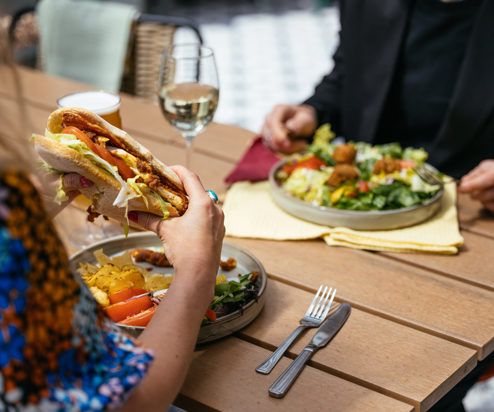 Two people sat outside eating hearty food dishes with a white wine and a pint of beer
