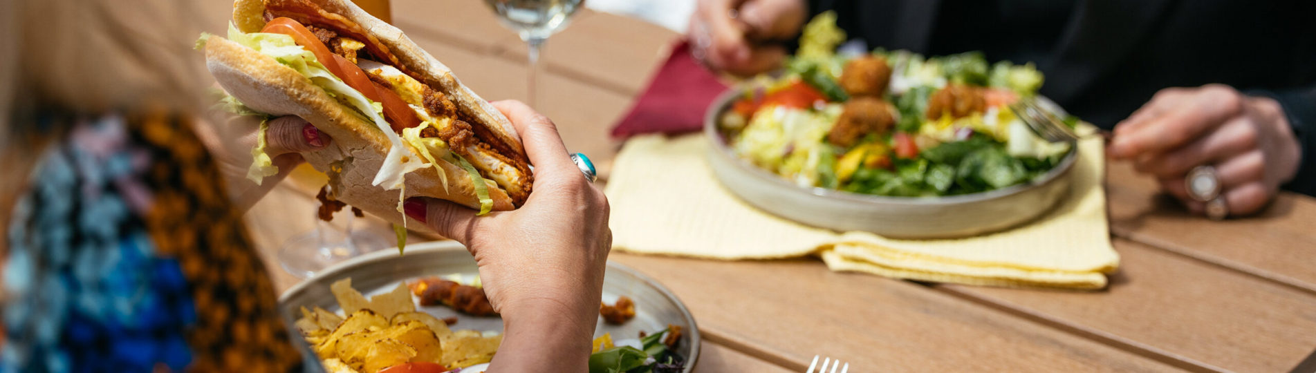 Two people sat outside eating hearty food dishes with a white wine and a pint of beer