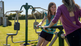 A young girl and a woman on outdoor gym equipment in a field