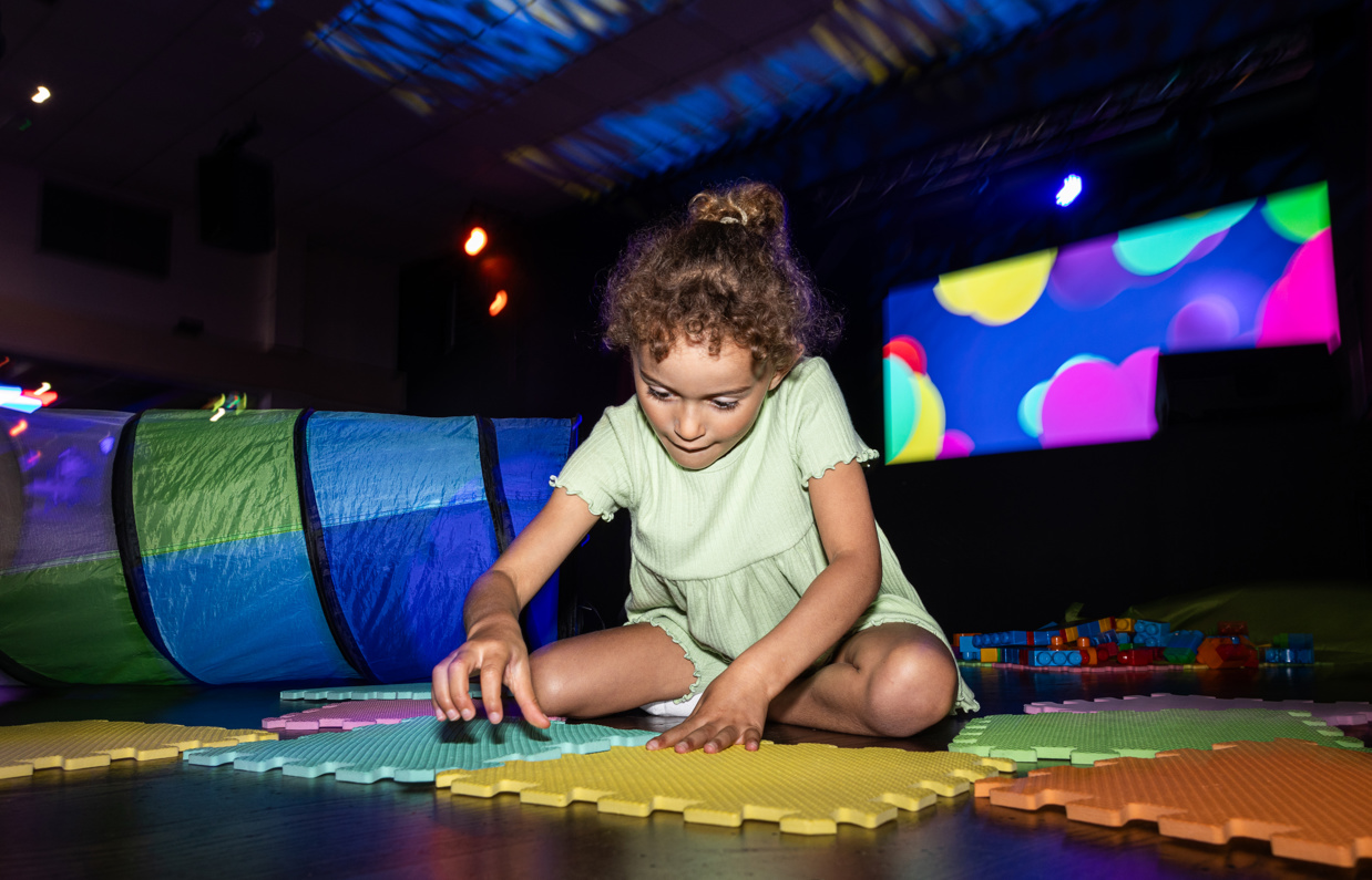 A young girl sat on the floor of an entertainment venue playing with soft play toys
