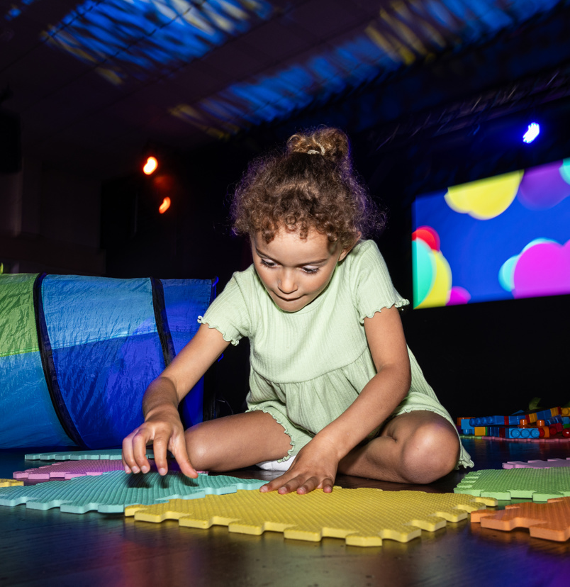 A young girl sat on the floor of an entertainment venue playing with soft play toys
