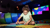 A young girl sat on the floor of an entertainment venue playing with soft play toys