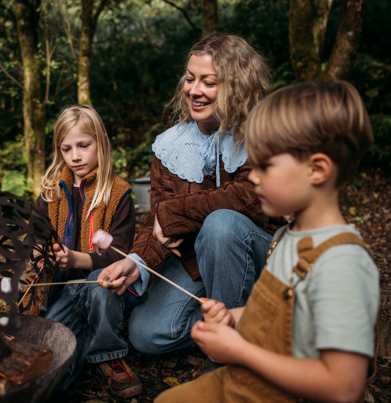 A mother and two young boys toasting marshmallows outside on a firepit