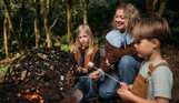 A mother and two young boys toasting marshmallows outside on a firepit