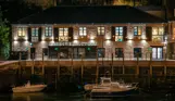 The external of The Sardine Factory restaurant lit up at night alongside the water with boats