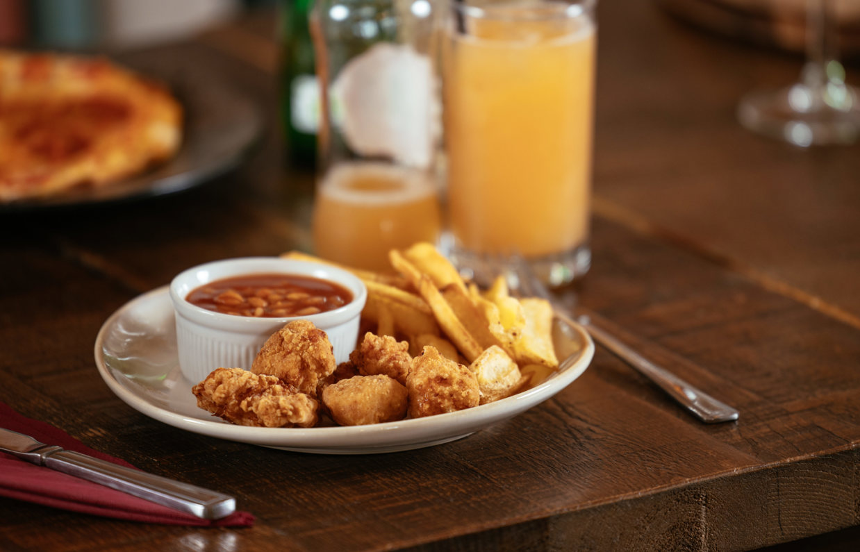 A plate of children's food on a table with a pizza and drinks