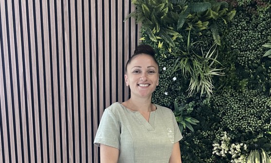A lady smiling in spa uniform against a greenery / walnut decór background