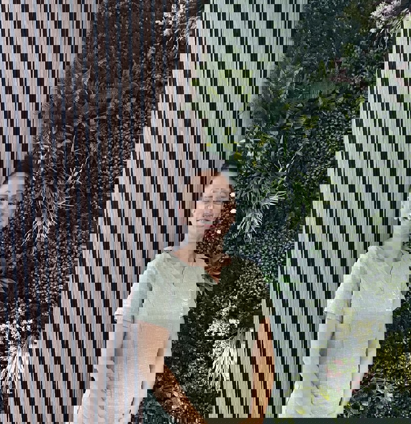 A lady smiling in spa uniform against a greenery / walnut decór background