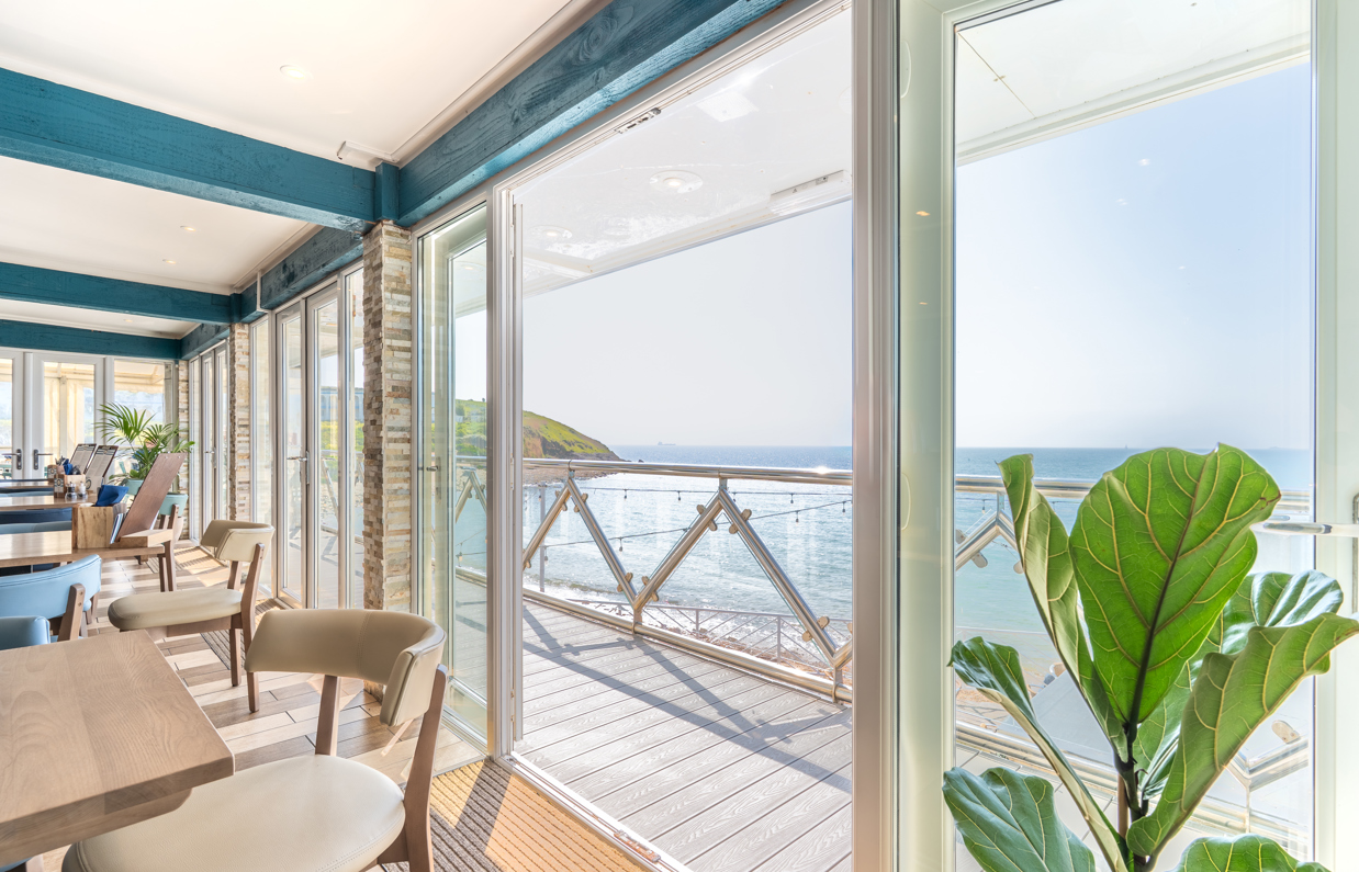 Views out to sea and coast from Drift Bar & Grill's seating area through wide open french doors on a sunny, blue sky day