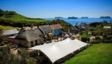 Aerial view of a quaint cottage-style pub with a thatched roof on the coast with countryside and sea views with cruise ships in the distance