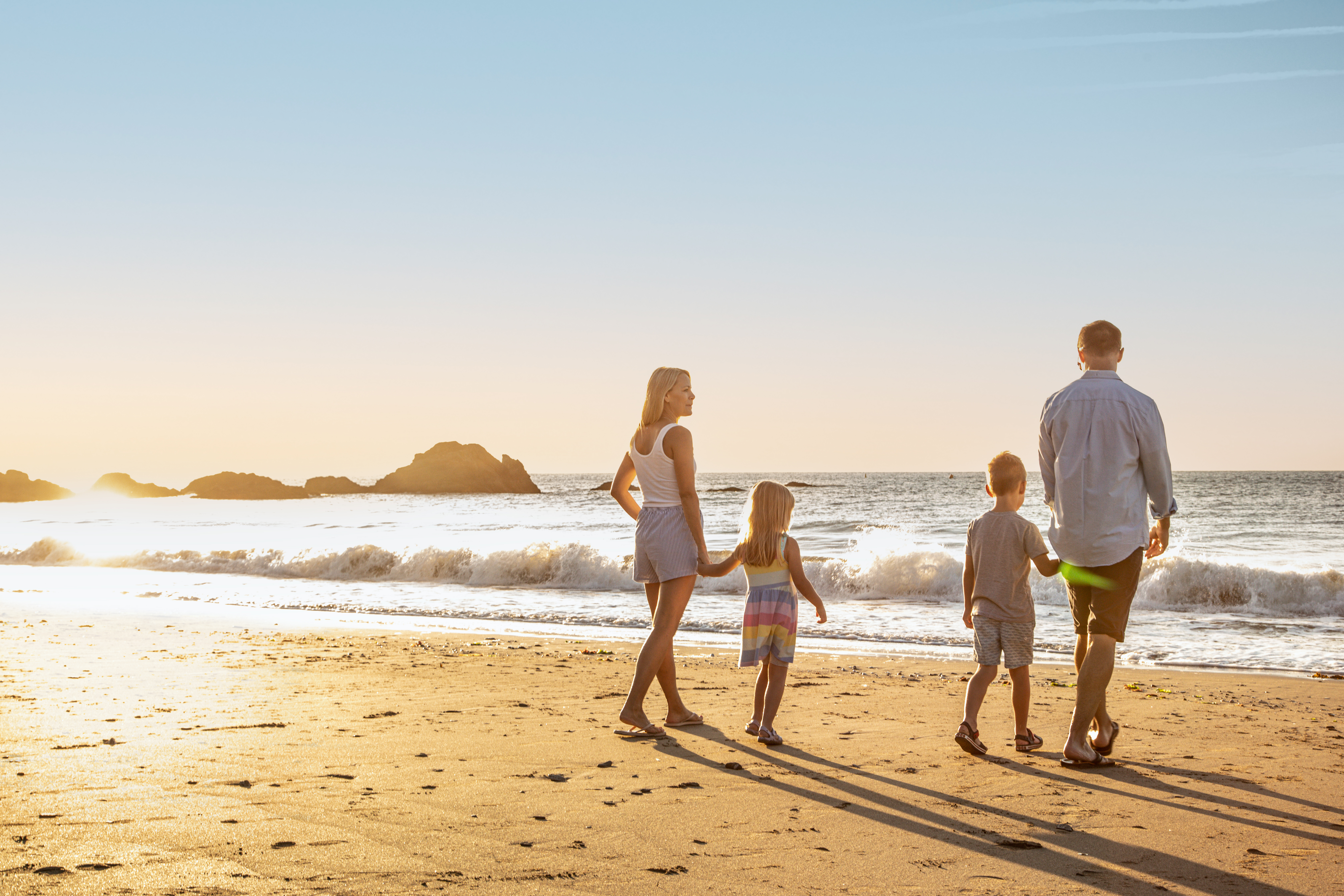 A family of four walking along the beach by the sea at sunrise with rocky mounds in the distance