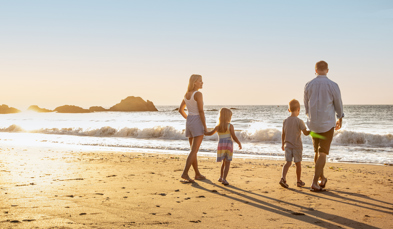 A family of four walking along the beach by the sea at sunrise with rocky mounds in the distance