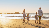 A family of four walking along the beach by the sea at sunrise with rocky mounds in the distance