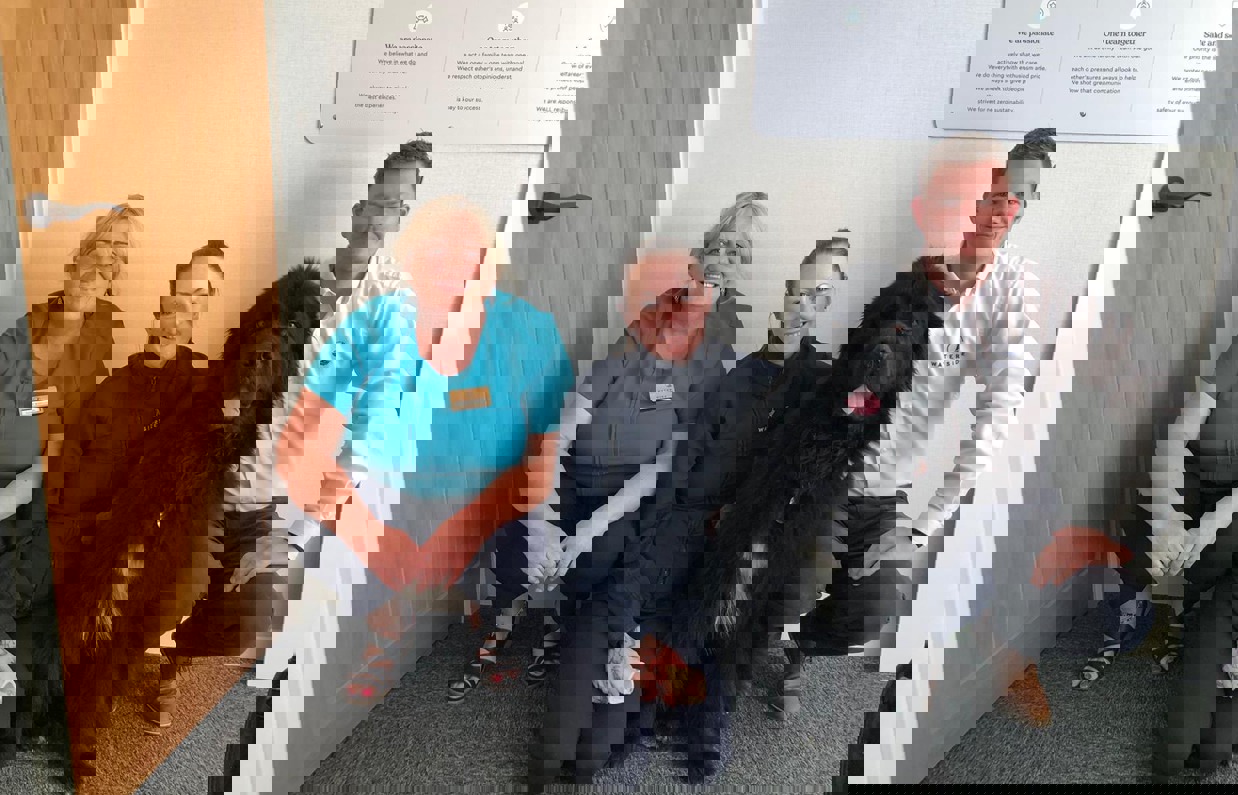 Three adults sat beside a large black dog after completing dog first aid training