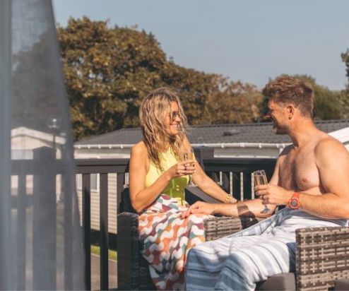 A couple sat on the balcony of a holiday home with champagne smiling at each other