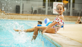 A young girl sat on the edge of an indoor swimming pool splashing her legs in the water