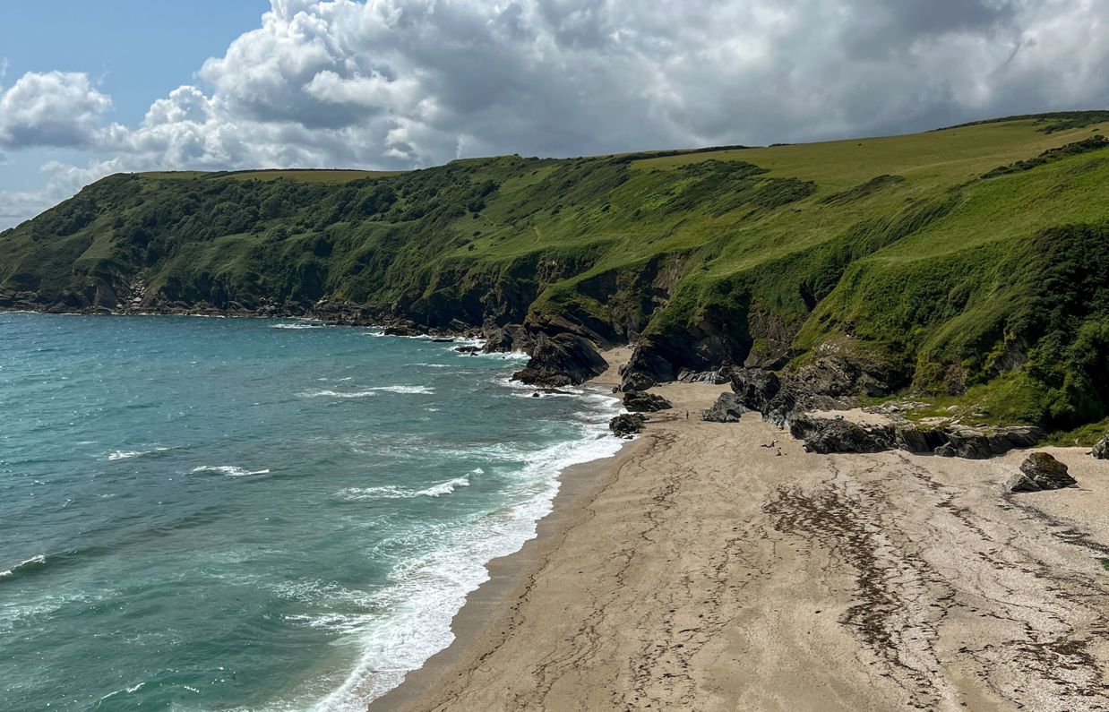 A small bay at the bottom of rolling countryside hills with blue water