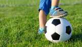 A child's foot on a football in a field