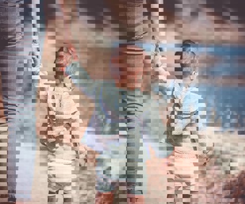 A young toddler walking along with coast holding an adult's hand