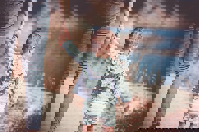 A young toddler walking along with coast holding an adult's hand