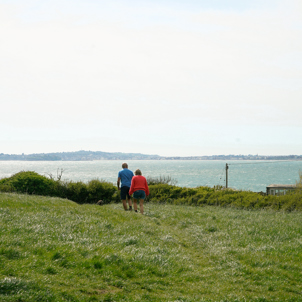 A couple and a dog walking along the coast path with the sea, Weymouth and Portland in distance