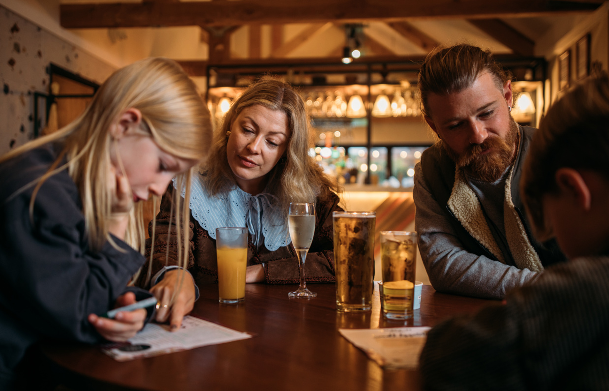 A couple with their two sons sat at a table in Stargazy Bar & Grill looking at a worksheet with drinks on the table