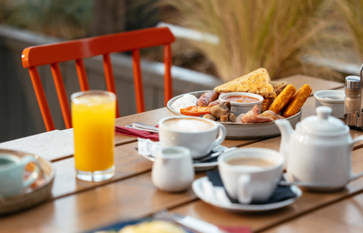 A full English breakfast on an outdoor table with various breakfast drinks