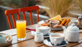 A full English breakfast on an outdoor table with various breakfast drinks
