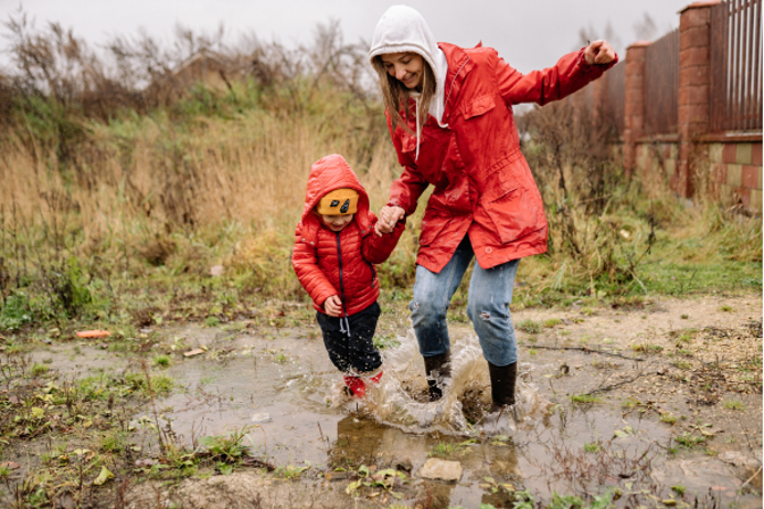 A woman and a child in rain gear splashing in muddy puddles