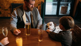 A young boy and his Dad sat at a table in Stargazy Bar & Grill with drinks and feeding a dalmatian dog ice cream