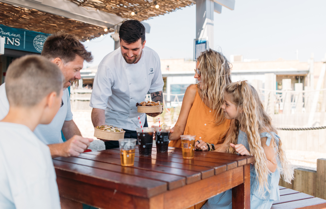 A chef serving a family of four street food at an outside table