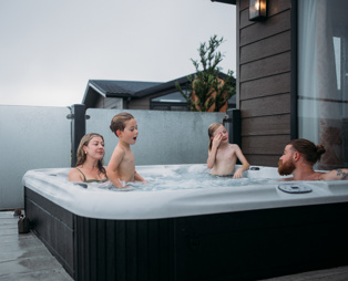 A family of four in a hot tub of a luxury lodge at Tregoad Holiday Park on a grey day
