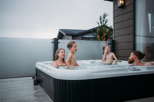 A family of four in a hot tub of a luxury lodge at Tregoad Holiday Park on a grey day